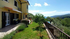 A yellow building with a balcony, a stone pathway, and a view of the hills.
