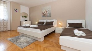 A hotel room with a large bed, two bedside tables, a nightstand, a small table with a vase, and a painting on the wall.