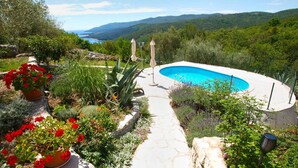 A pool surrounded by a garden with a stone pathway leading to it.