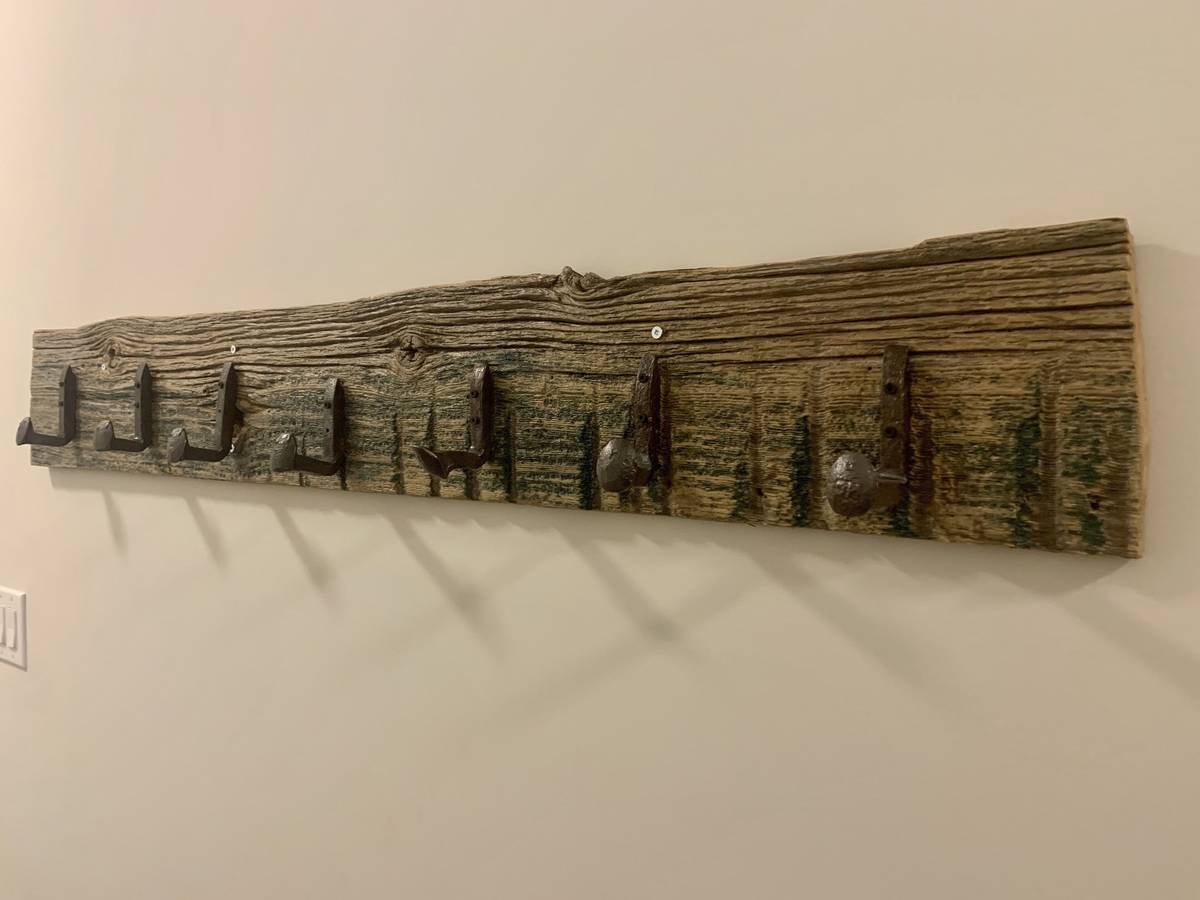 A wall-mounted wooden artwork with metal hooks.