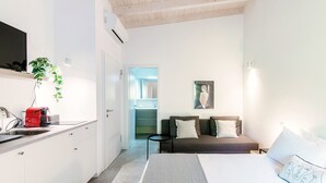 Habitació d'hotel moderna amb un llit, un sofà, una taula petita i una cuina amb un aparell vermell.