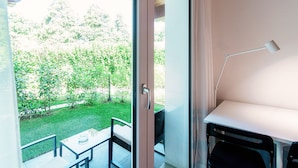 Une pièce dotée d’une porte-fenêtre coulissante donnant sur un balcon avec vue sur un jardin verdoyant.