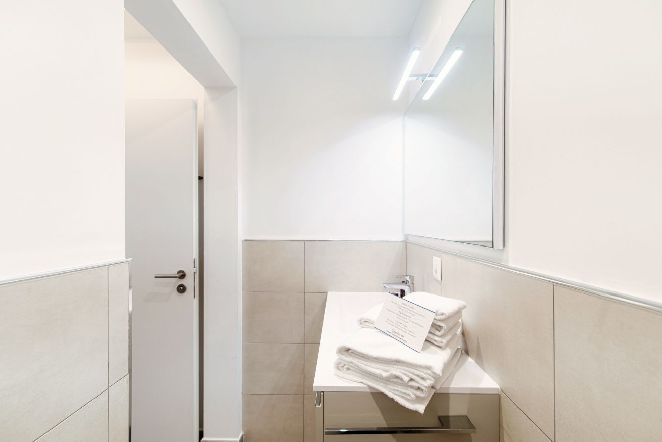 Ein modernes Badezimmer mit einem weißen Waschbecken, einem Spiegel und einem Handtuchhalter.