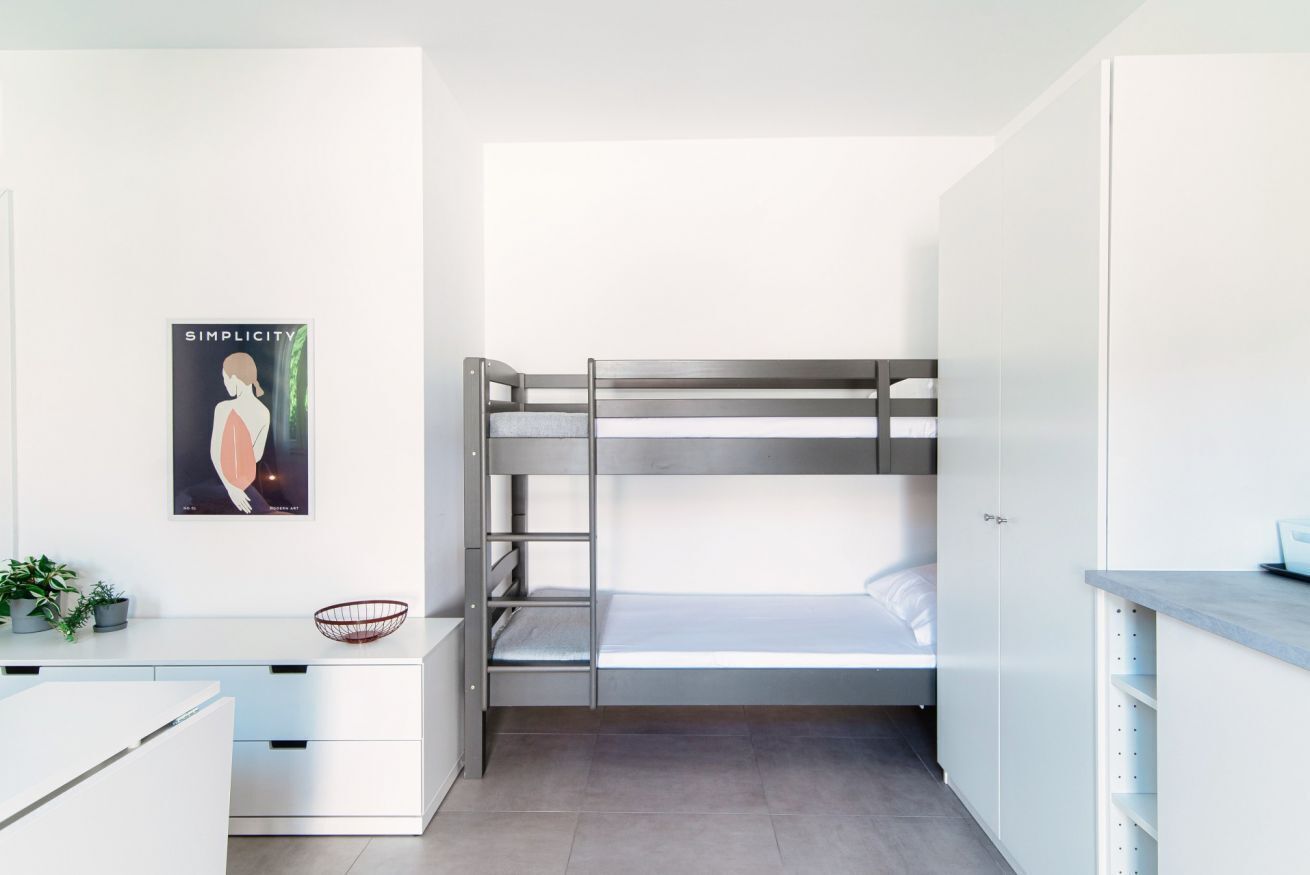 Ein kompakter, moderner Schlafraum mit Etagenbett, weißem Schreibtisch und minimalistischem Design.