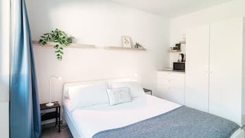 A bedroom with a bed, bedside table, lamp, and a small desk with a kettle.