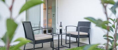 An outdoor seating area with two chairs and a table, a bottle of wine, and a glass.