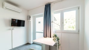 Ett modernt, minimalistiskt rum med en platt-TV som är monterad på väggen, ett skrivbord med en stol, en golvlampa och en krukväxt.