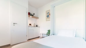 Ett minimalistiskt sovrum med en säng, ett litet sängbord och en vägghylla med köksartiklar.