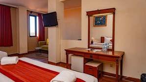 A hotel room with a bed, a desk, a chair, a television, and a painting on the wall. - Puri Dibia Hotel (Kuta)