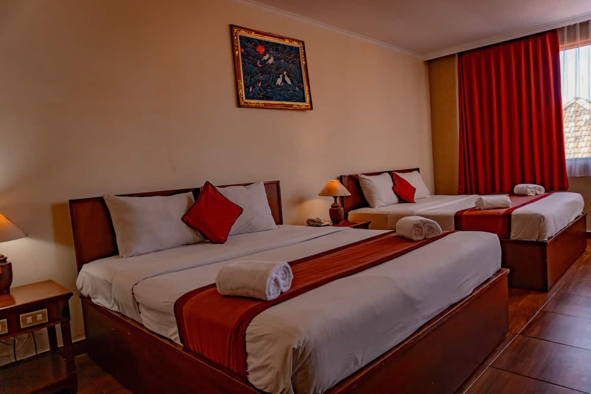 A hotel room with three beds, each with white linens and red accents, a wooden headboard, and a painting on the wall.