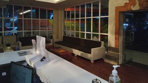 A hotel lobby with a reception desk, seating area, and large windows offering views of the outside. - Puri Dibia Hotel (Kuta)