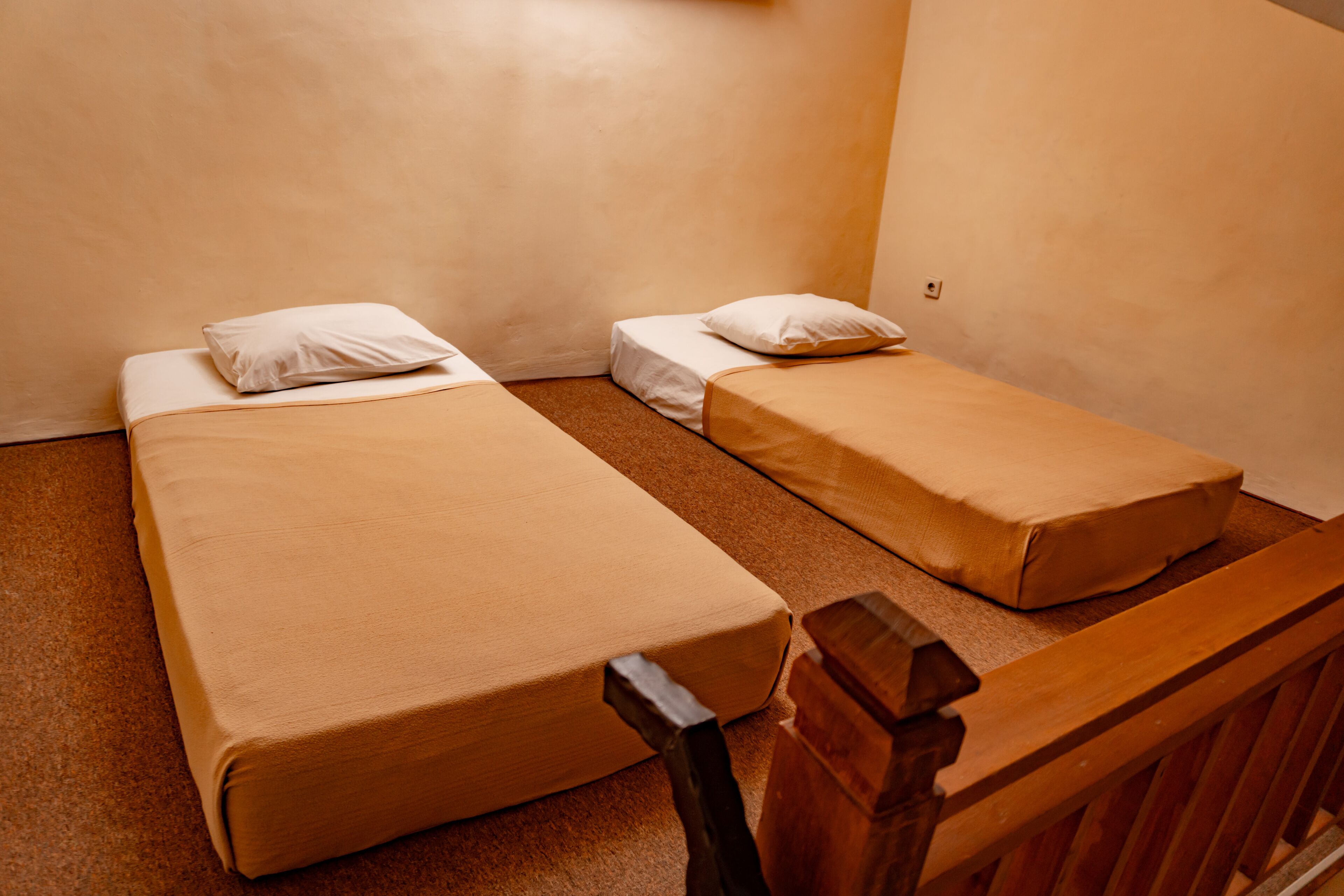 Une petite chambre d’hôtel composée d’une seule pièce, avec deux lits simples, chacun muni d’un oreiller et d’un protège-matelas uni.