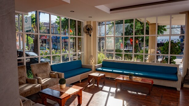 A spacious room with large windows, a blue sofa, and wooden furniture. - Puri Dibia Hotel (Kuta)