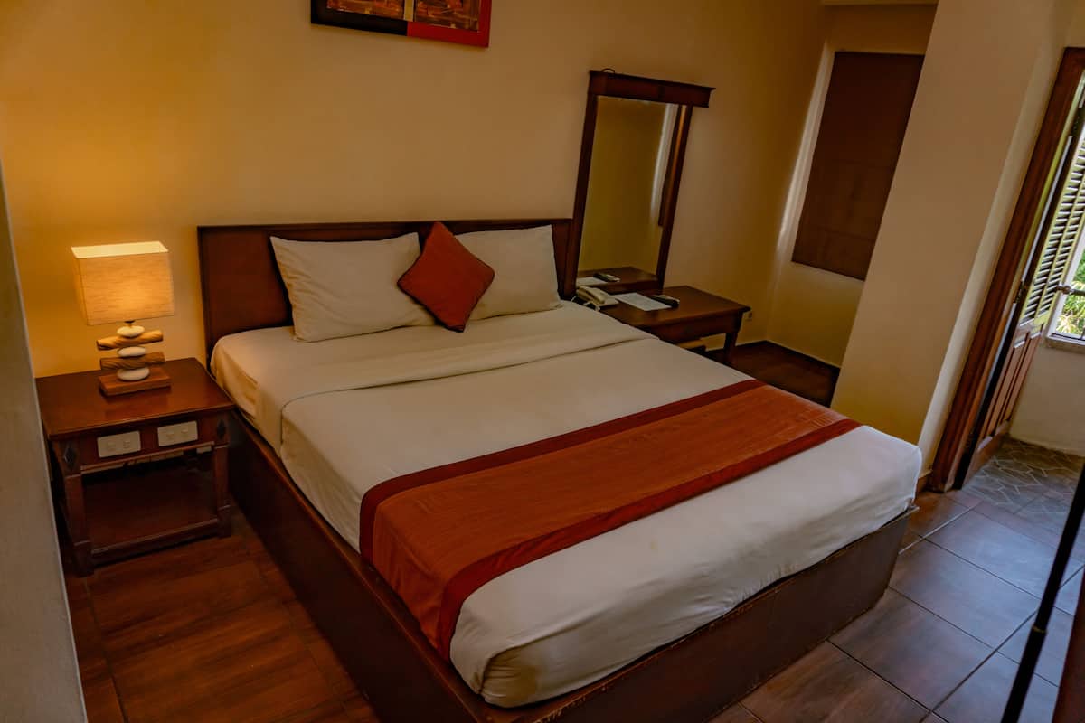 A hotel room with a large bed, a nightstand with a lamp, a mirror, and a window with a view.