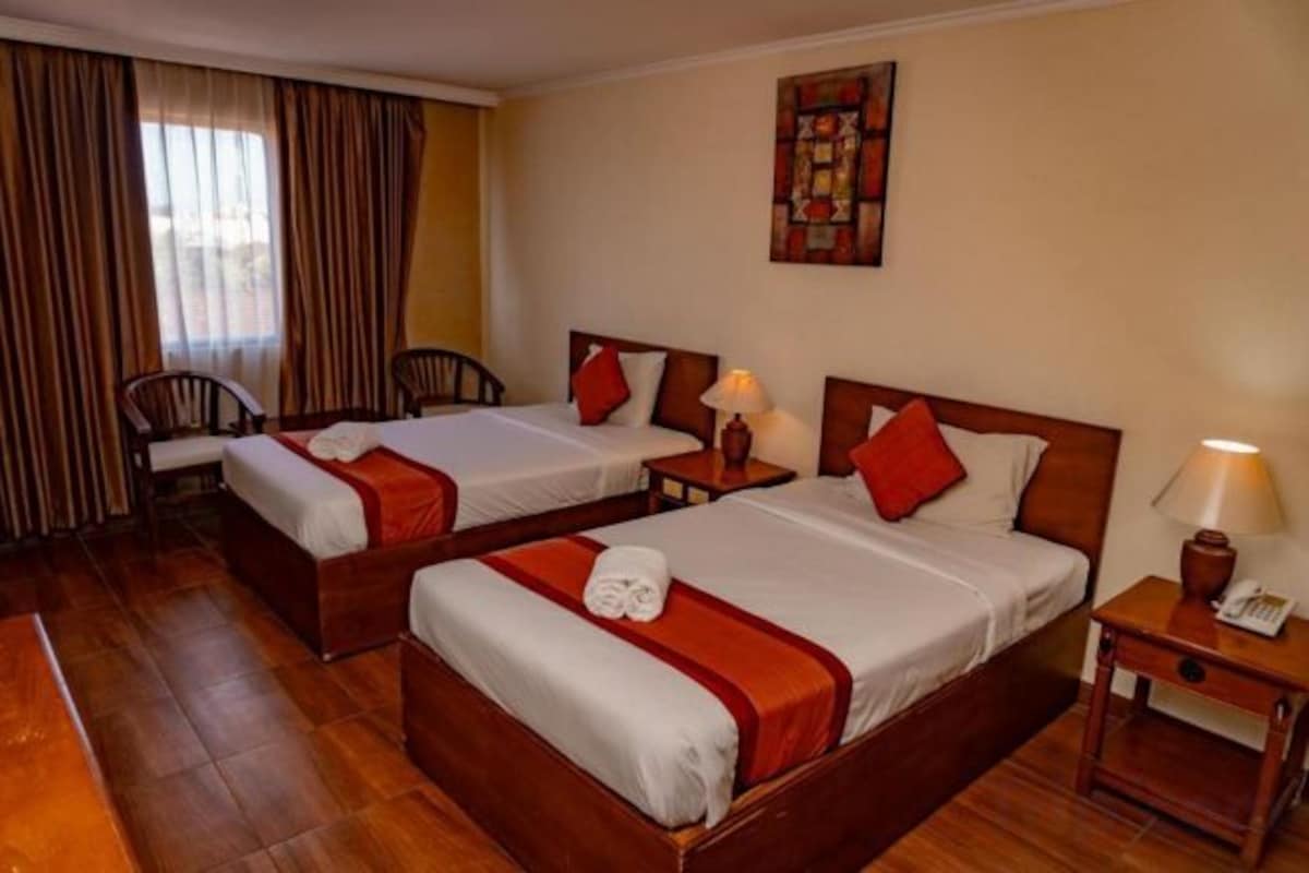 Una habitación de hotel con dos camas individuales, un escritorio, una silla y una mesita de noche con lámpara.