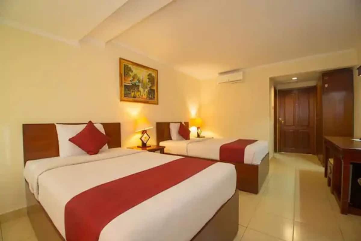 A hotel room with two beds, a wooden headboard, a painting on the wall, and a desk with a chair.
