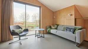 A modern room with a large window, a black chair, a small round table, and a grey sofa with patterned cushions. - 3 bedroom awesome home in Spier (Spier)