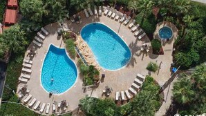 Vista aerea di un resort con due grandi piscine circondate da lettini e palme.