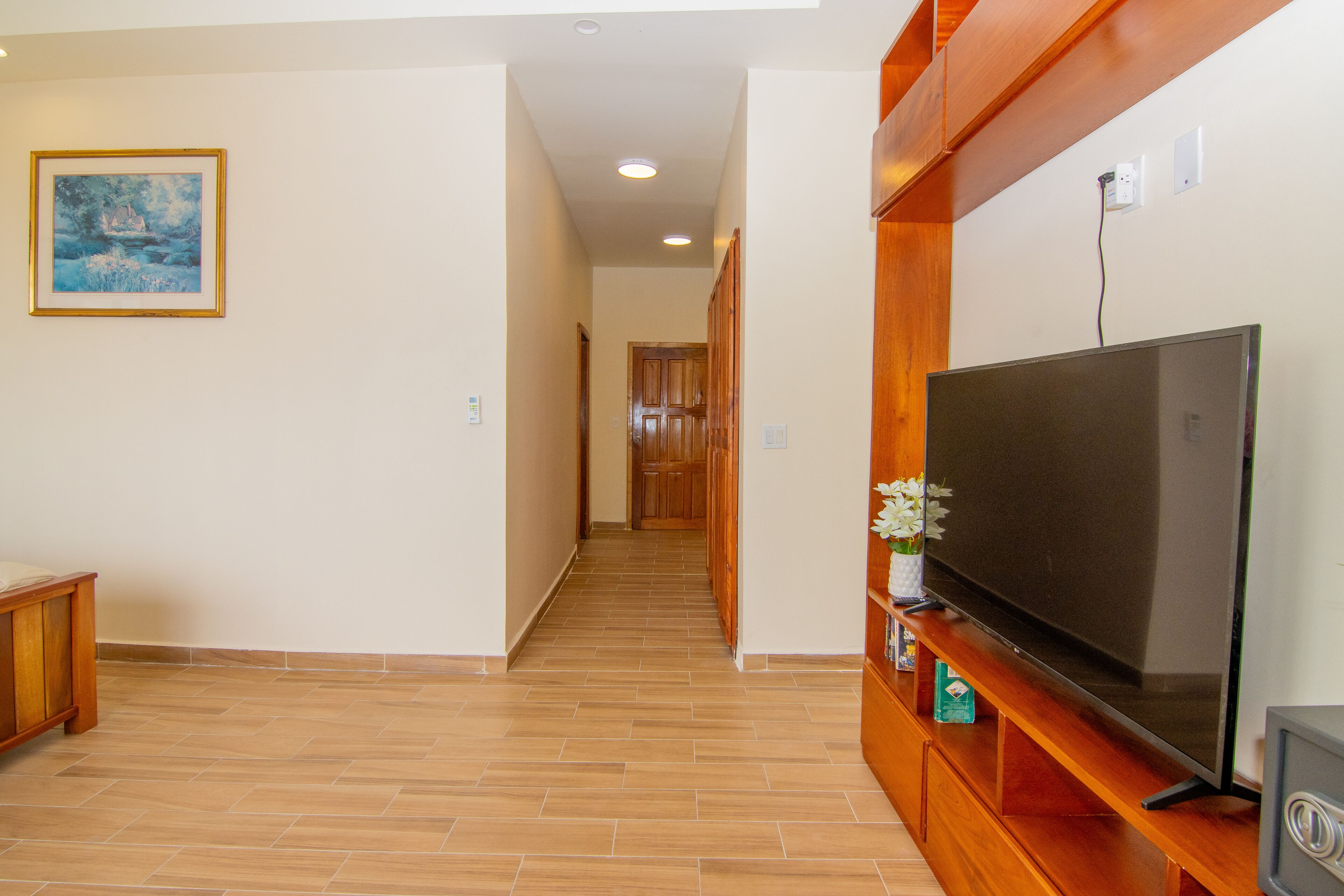 A hallway with a wooden entertainment unit, a television, and a framed painting on the wall.