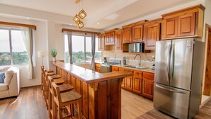 A modern kitchen with wooden cabinets, a stainless steel refrigerator, and a bar area with stools. - Tropical Palace Hotel (San Pedro)
