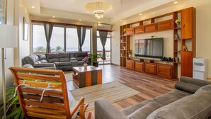 A spacious living room with a large flat-screen TV, wooden cabinets, and a comfortable seating area. - Tropical Palace Hotel (San Pedro)