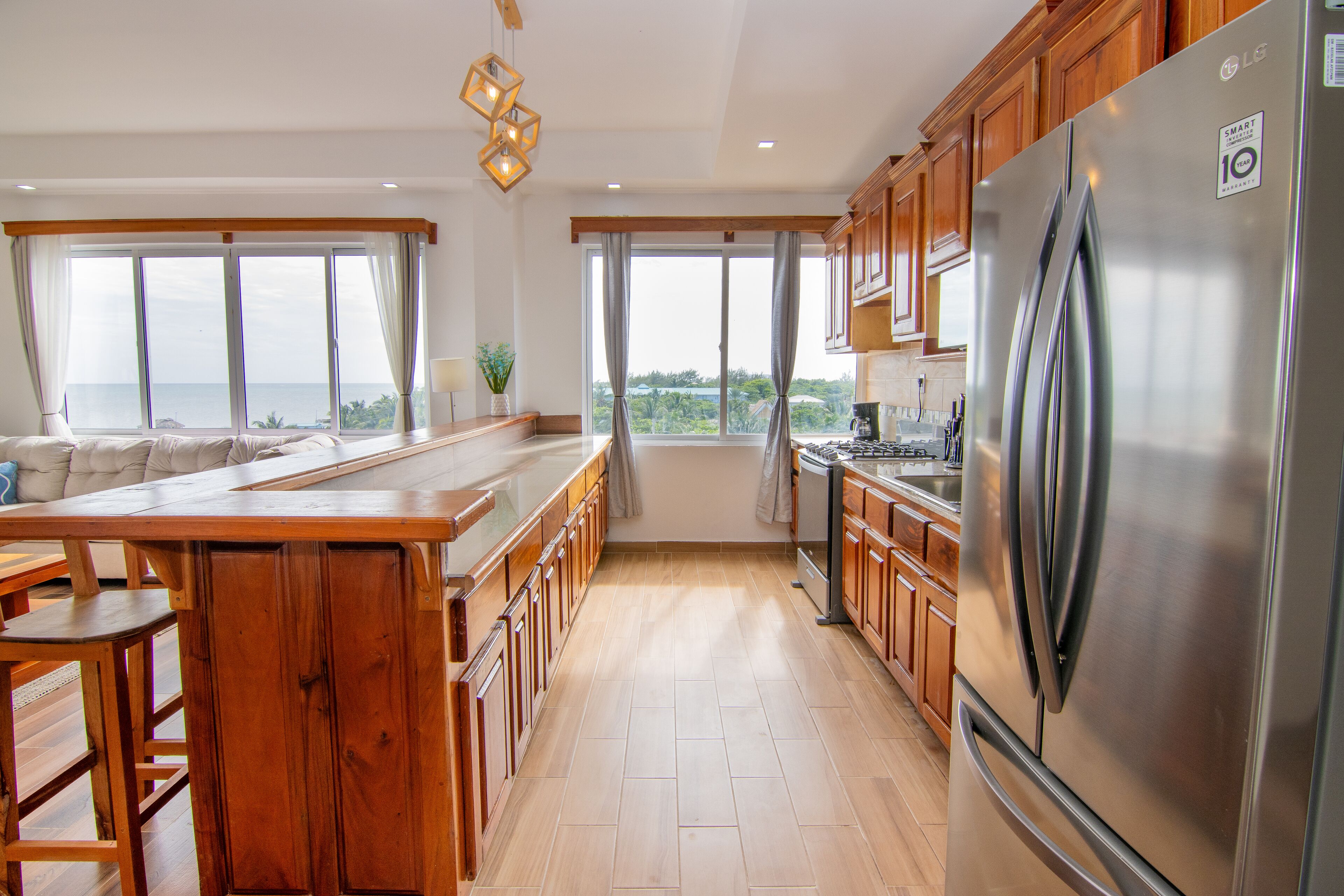 A modern kitchen with wooden cabinets, a stainless steel refrigerator, and a large island with bar stools.