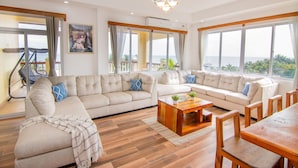 A spacious living room with a large sectional sofa, a wooden coffee table, and a dining area with wooden chairs. - Tropical Palace Hotel (San Pedro)