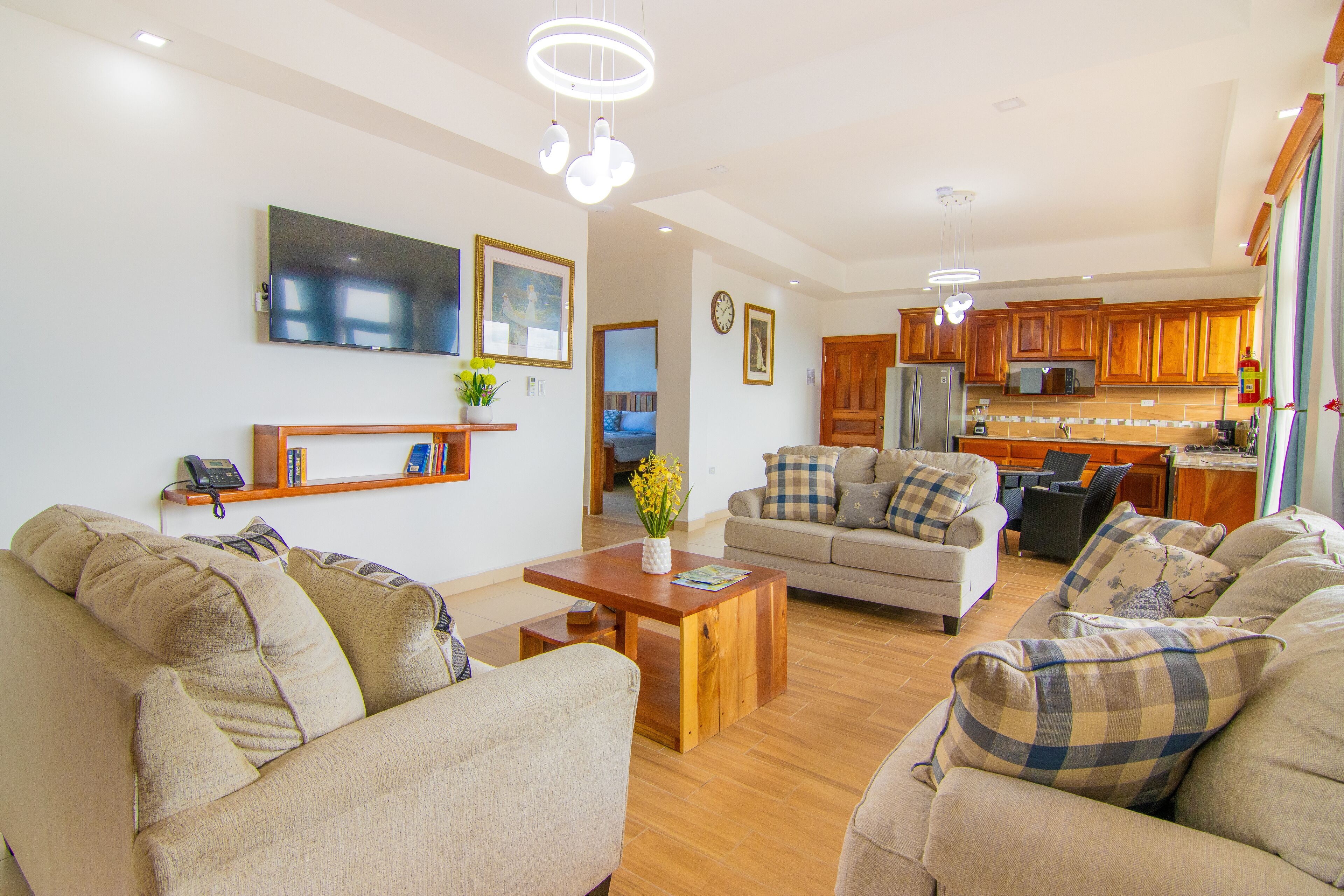 A spacious living room with a sofa set, a coffee table, and a television mounted on the wall.