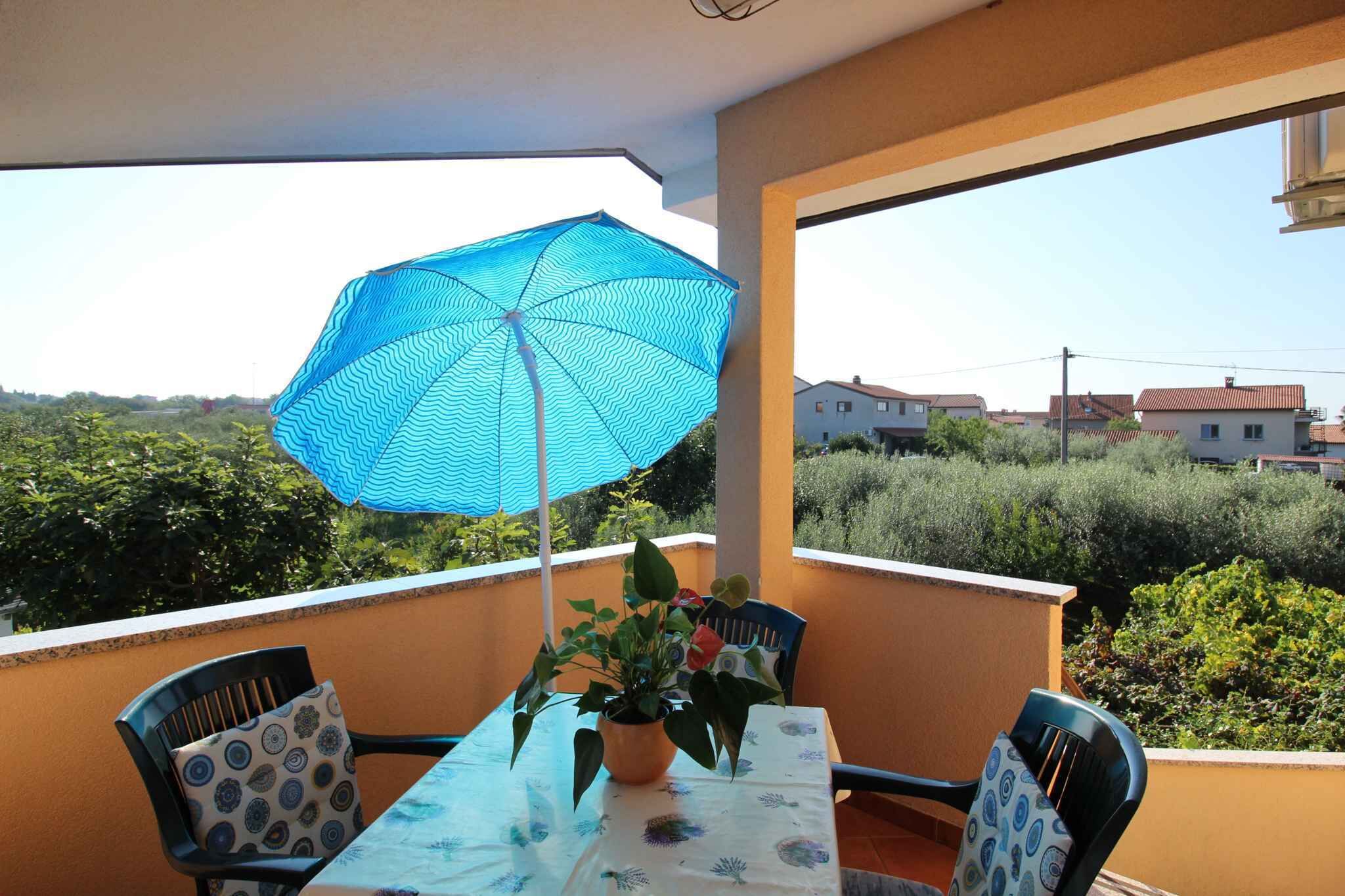 Een balkon met een tafel, stoelen, een bloempot en een blauwe parasol.