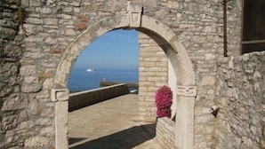 Un arc en pierre mène à un point de vue sur la côte, où l’on aperçoit un navire au loin.