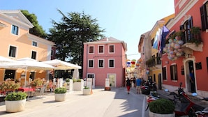 Une rue avec des terrasses, un bâtiment rose et des scooters garés.
