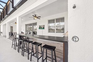A modern outdoor kitchen area with a bar, high chairs, and a ceiling fan. - 15BR/15.5BA Kissimmee Resort Villa w/ Stunning Clubhouse (Kissimmee)