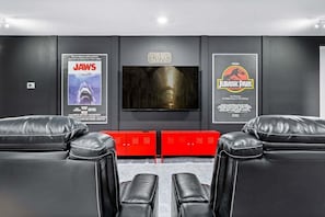 A home theater with leather recliners, a TV, and movie posters for 'Jaws' and 'Jurassic Park'.