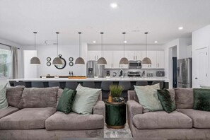 A modern kitchen with pendant lighting, a central island, and a dining area with two sofas.