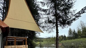 Puinen terassi, jossa on pöytä ja tuoleja, puinen aita ja näkymä joelle ja metsään.