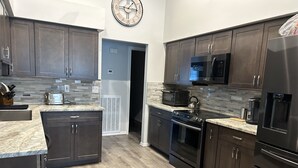 Una cocina moderna con armarios de madera oscura, encimera de granito, electrodomésticos de acero inoxidable y un reloj en la pared.