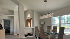 Un comedor moderno con una mesa y sillas de vidrio, una araña y vistas al exterior.