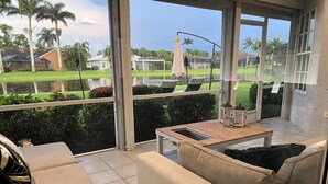 Un espacio de patio techado con vistas a un barrio residencial, que incluye casas y palmeras.