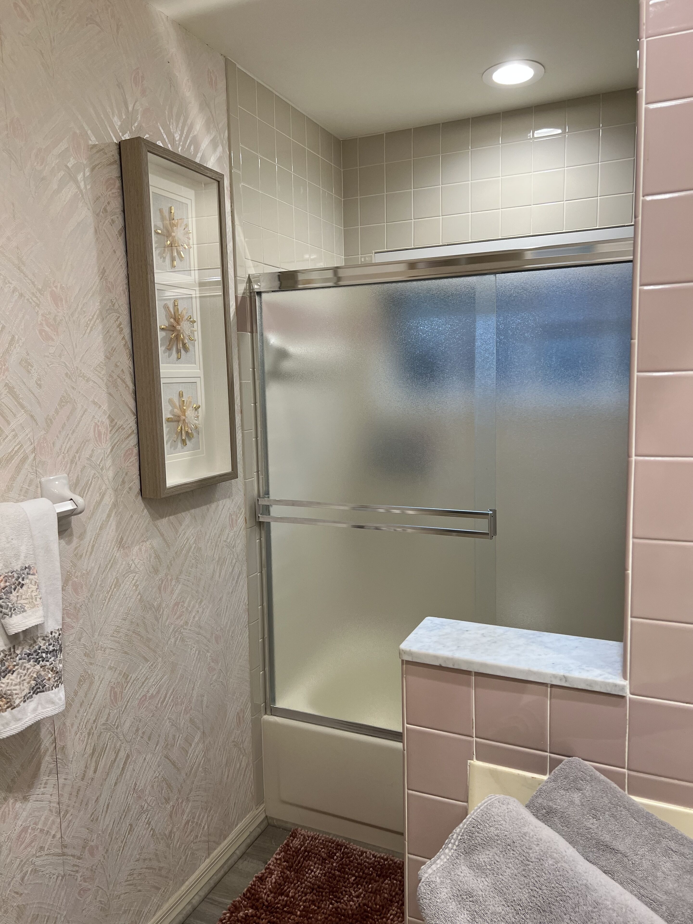 Une salle de bain moderne avec une douche à parois de verre, un tableau encadré au mur et un comptoir en marbre.