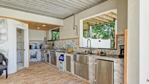 A spacious kitchen with a brick floor, built-in appliances, and a large window overlooking greenery. - Serenity Cottage in Anna Maria (Anna Maria)