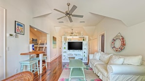 A living room with a white sofa, a green bench, a TV, and a ceiling fan. - Serenity Cottage in Anna Maria (Anna Maria)