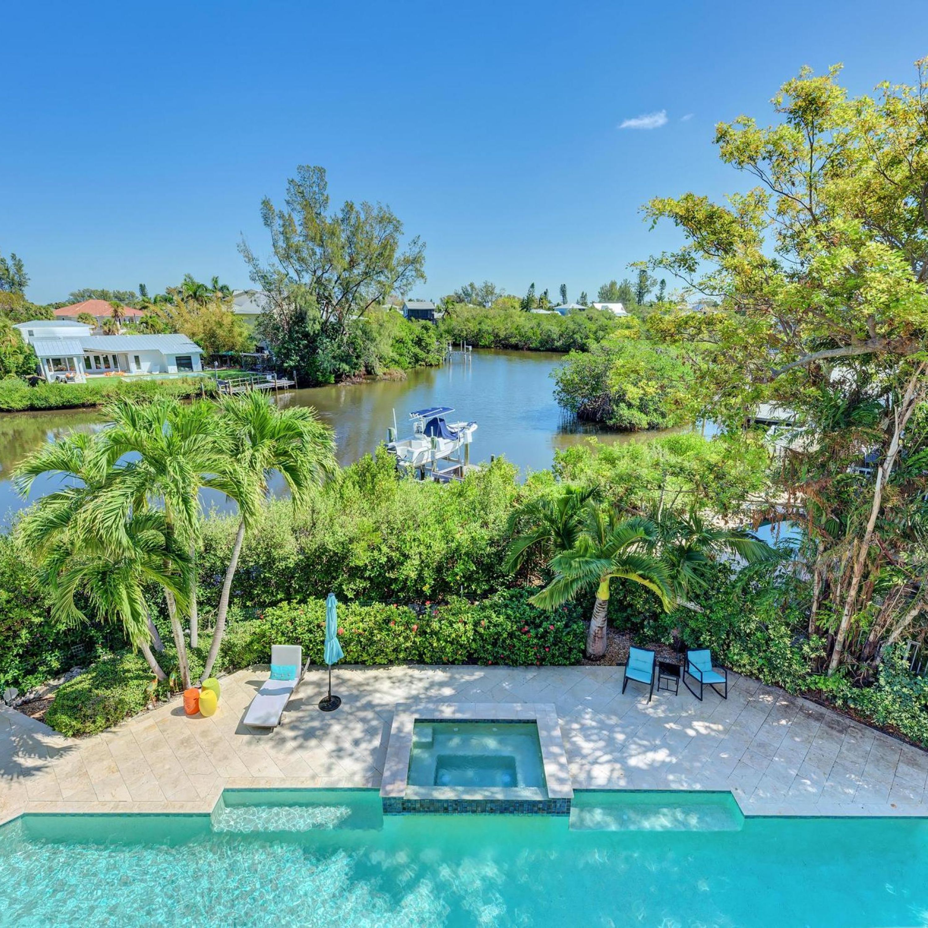 Zona de piscina con vista a un río y barcos, rodeada de exuberante vegetación y palmeras.