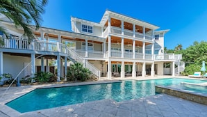 A two-story house with a large swimming pool, multiple balconies, and outdoor seating areas. - Serenity Cottage in Anna Maria (Anna Maria)