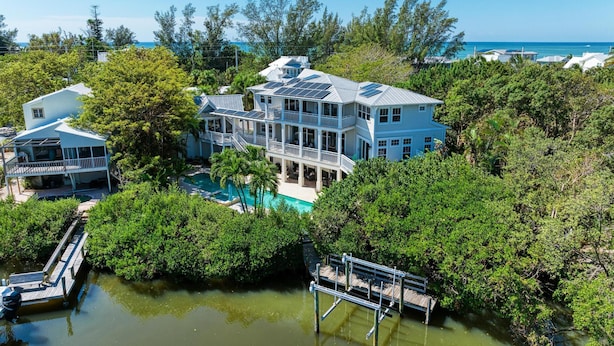 A large, multi-story house with a pool surrounded by dense greenery and a clear view of the ocean. - Serenity Cottage in Anna Maria (Anna Maria)