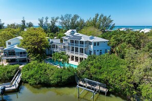 A large, multi-story house with a pool surrounded by dense greenery and a clear view of the ocean. - Serenity Cottage in Anna Maria (Anna Maria)