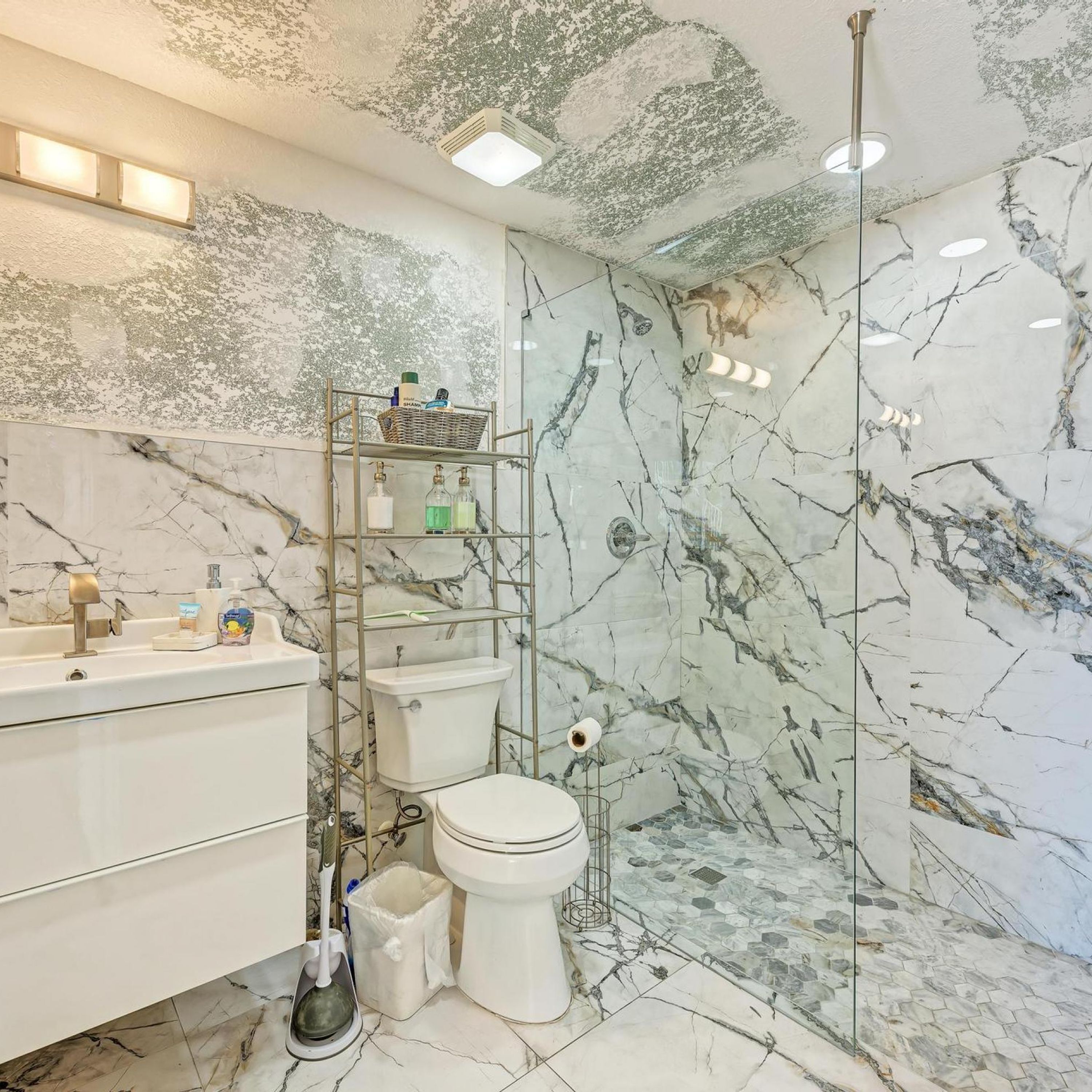 A bathroom with a marble floor, a white toilet, a sink with a mirror, and a shower area with a glass door.