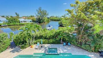 A swimming pool with a hot tub, surrounded by lush greenery and a view of a river.