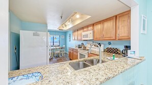 A kitchen with granite countertops, wooden cabinets, a microwave, and a sink. - AM Island Beach To Bay Bliss (Bradenton Beach)