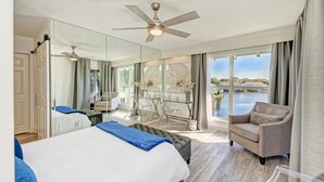 A modern hotel room with a large bed, a seating area with a chair and table, a ceiling fan, and a view of a body of water through large windows. - Perico Coastal Bay in Bradenton (Bradenton)