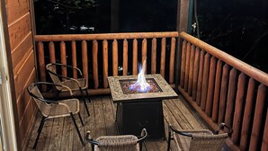 A wooden deck with a fire pit table, wicker chairs, and string lights. - 3 Bedroom, Sleeps 10, Close to town w Pool, Hot Tub, Sauna and Game Room! (Sevierville)